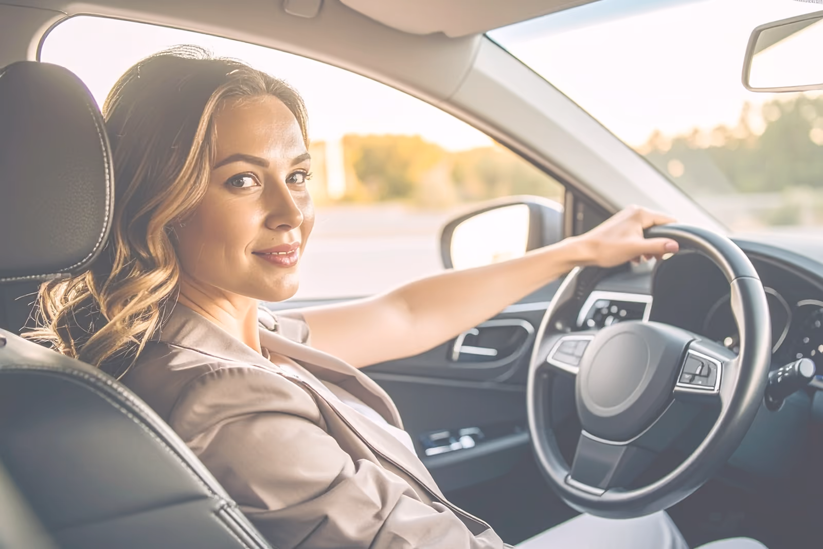 Smiling woman driving a car, looking toward the camera.